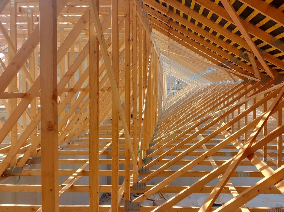 Structure en bois massif vue intérieure, charpente traditionnelle répétitive créant une perspective tunnel