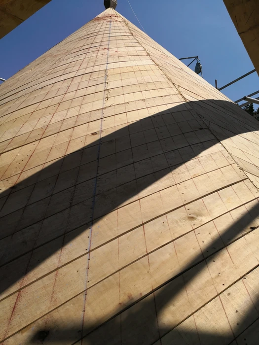 Vue en contre-plongée d'une structure conique en bois, prise depuis le bas vers le ciel bleu