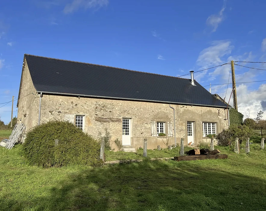 Longère rurale en pierre calcaire, toiture en ardoise noire récente, façade sud avec menuiseries blanches à petits carreaux, volets battants, porte d'entrée centrale