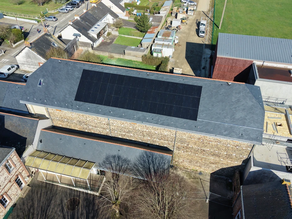 Vue aérienne par drone d'une toiture en ardoise avec installation de panneaux solaires photovoltaïques monocristallins noirs, disposés en matrice rectangulaire