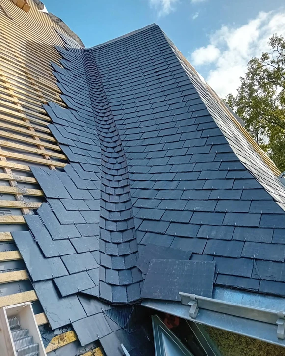 Ouvrier couvreur travaillant sur toiture ardoise d'une maison traditionnelle en pierre