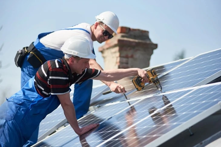 Ouvrier en équipement de sécurité installe des panneaux solaires photovoltaïques sur une toiture résidentielle par temps ensoleillé
