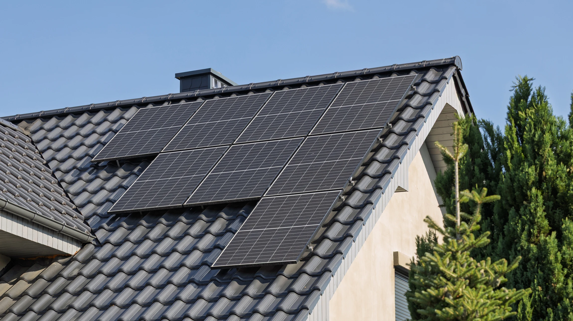 Ouvrier en tenue de sécurité haute visibilité et casque jaune installant des panneaux solaires photovoltaïques sur toiture résidentielle en bardeaux rouges, ciel bleu dégagé