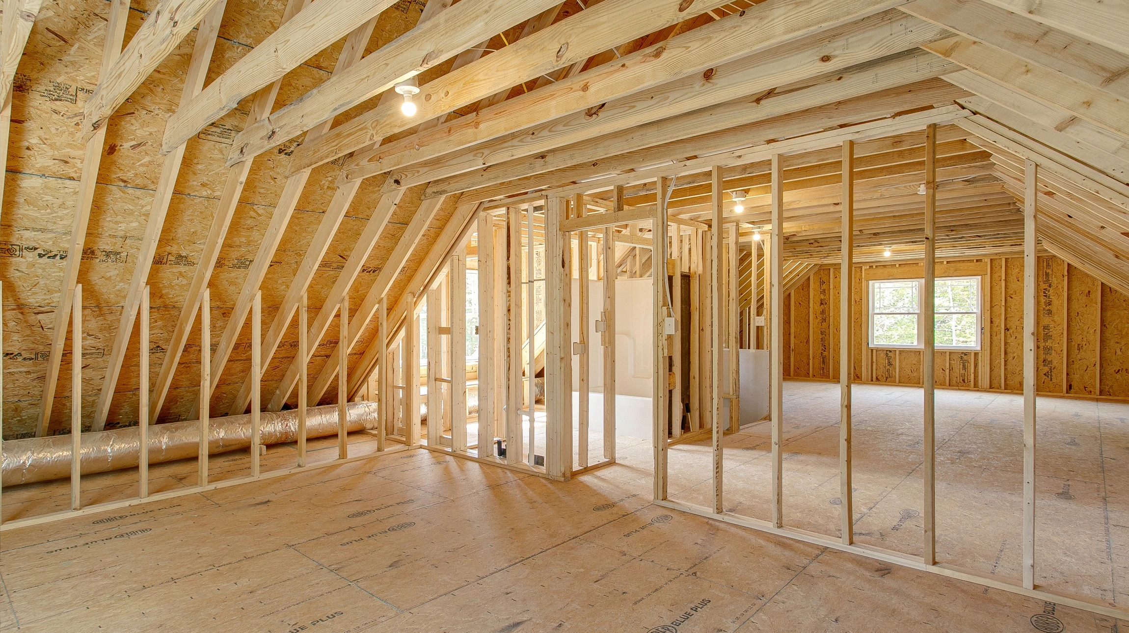 Intérieur de bâtiment en construction montrant une charpente en bois massif avec poutres, chevrons et fermes apparentes