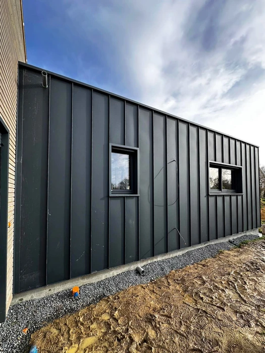 Vue aérienne d'un lotissement en construction, deux rangées de maisons individuelles en briques monomur rouge avec charpentes bois apparentes en cours de pose