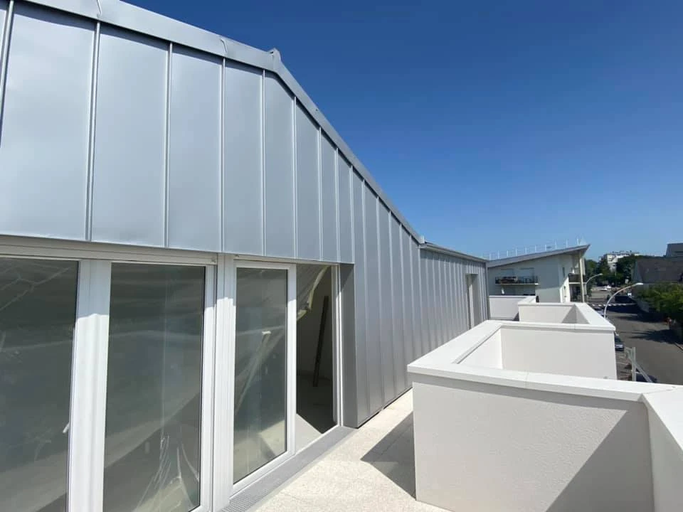 Toiture en ardoise naturelle grise, vue extérieure en contre-plongée, ciel bleu dégagé