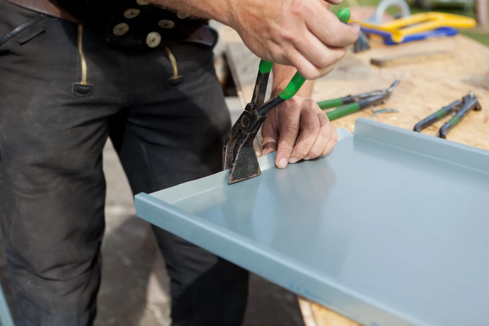 L'invention concerne un ouvrier de construction de toitures finissant de plier une tôle à l'aide d'une pince spéciale avec une grande poignée plate