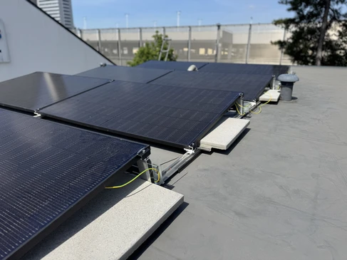 Deux techniciens en combinaisons rouges installent des panneaux solaires photovoltaïques sur une toiture de tuiles au coucher du soleil