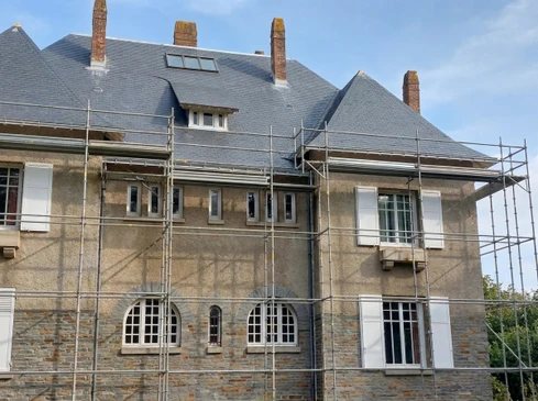 Ouvrier en équipement de sécurité orange et harnais installant une toiture métallique sur un bâtiment