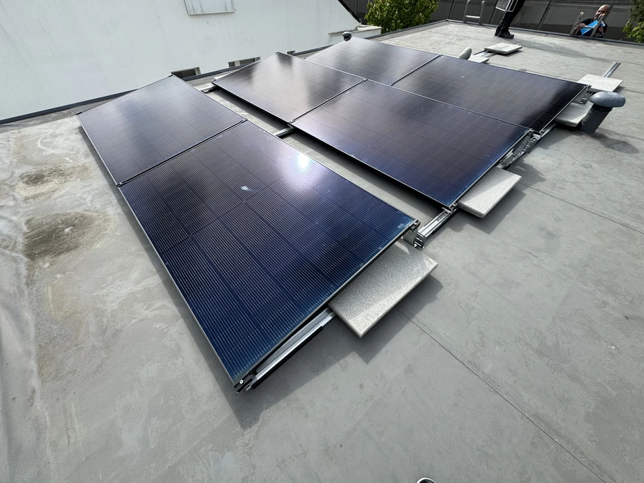 Toiture terrasse avec membrane EPDM grise, équipée de panneaux solaires photovoltaïques monocristallins noirs, montés sur ballasts d'inclinaison fixes