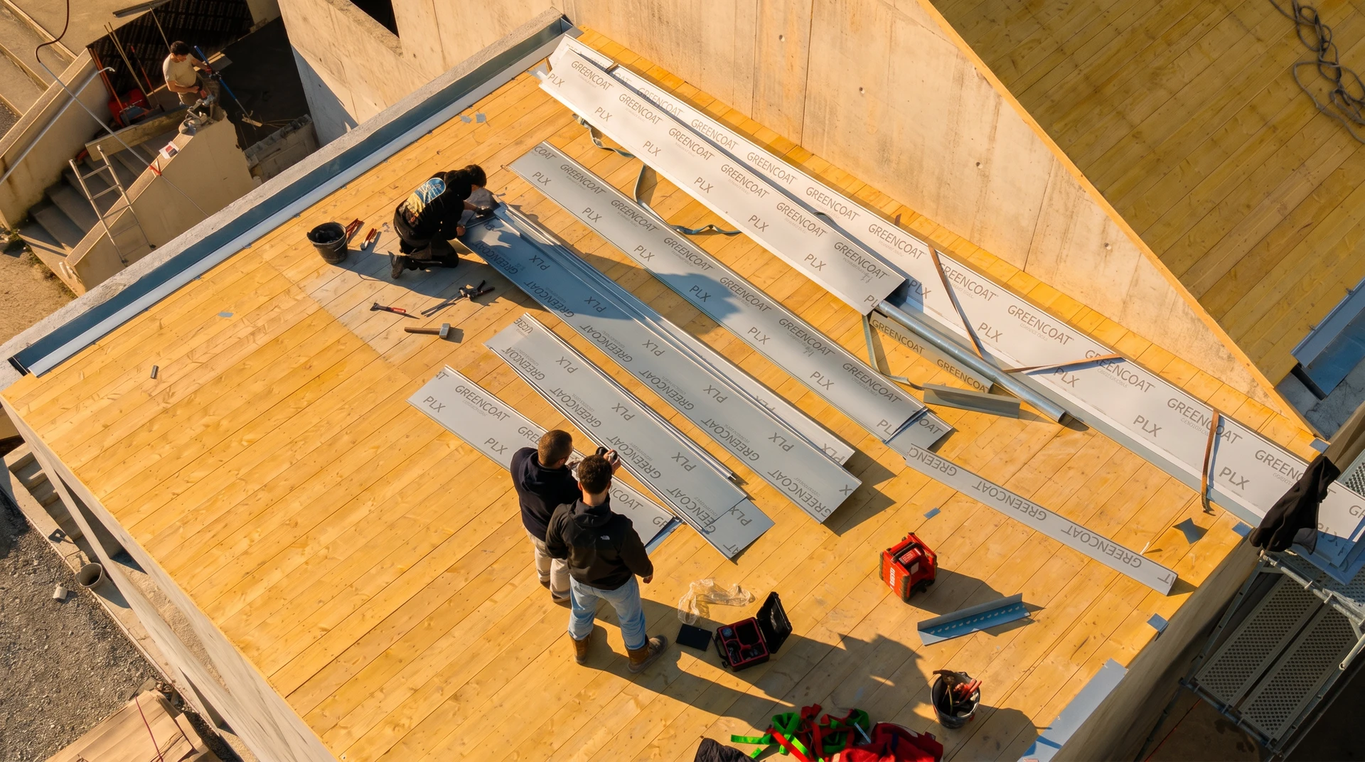Deux couvreurs professionnels travaillent sur une toiture en chantier au coucher du soleil